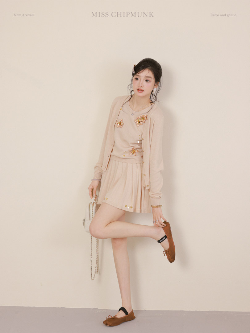 Model wearing a light beige cardigan and matching skirt set with floral accents and brown flats