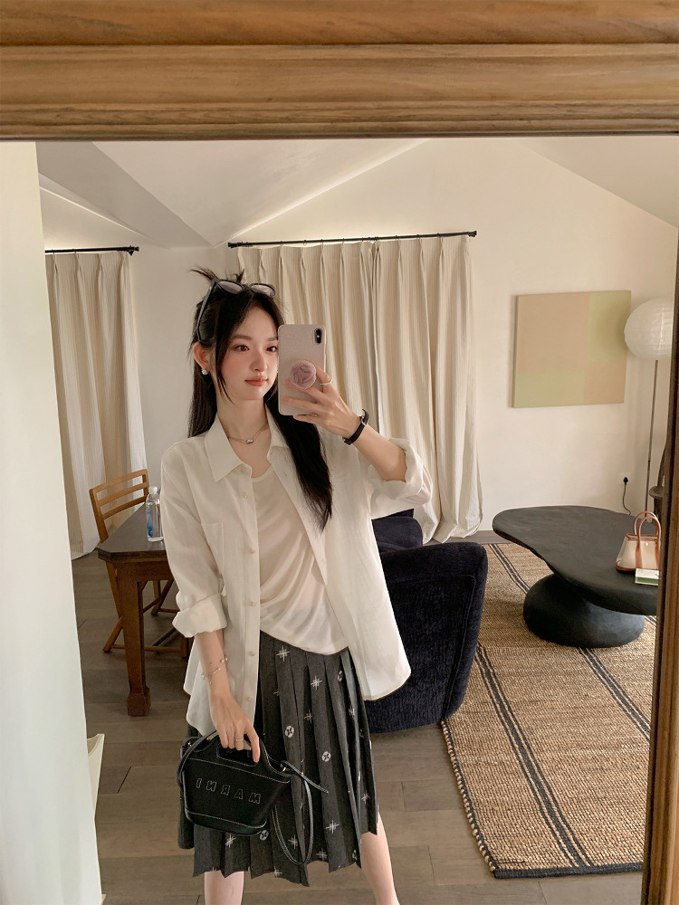 Woman wearing a white button-up shirt with a dark pleated skirt in a mirror selfie