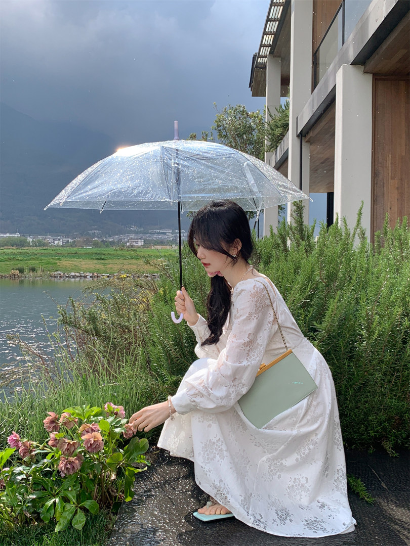 Woman wearing a white lace dress outdoors while holding a clear umbrella