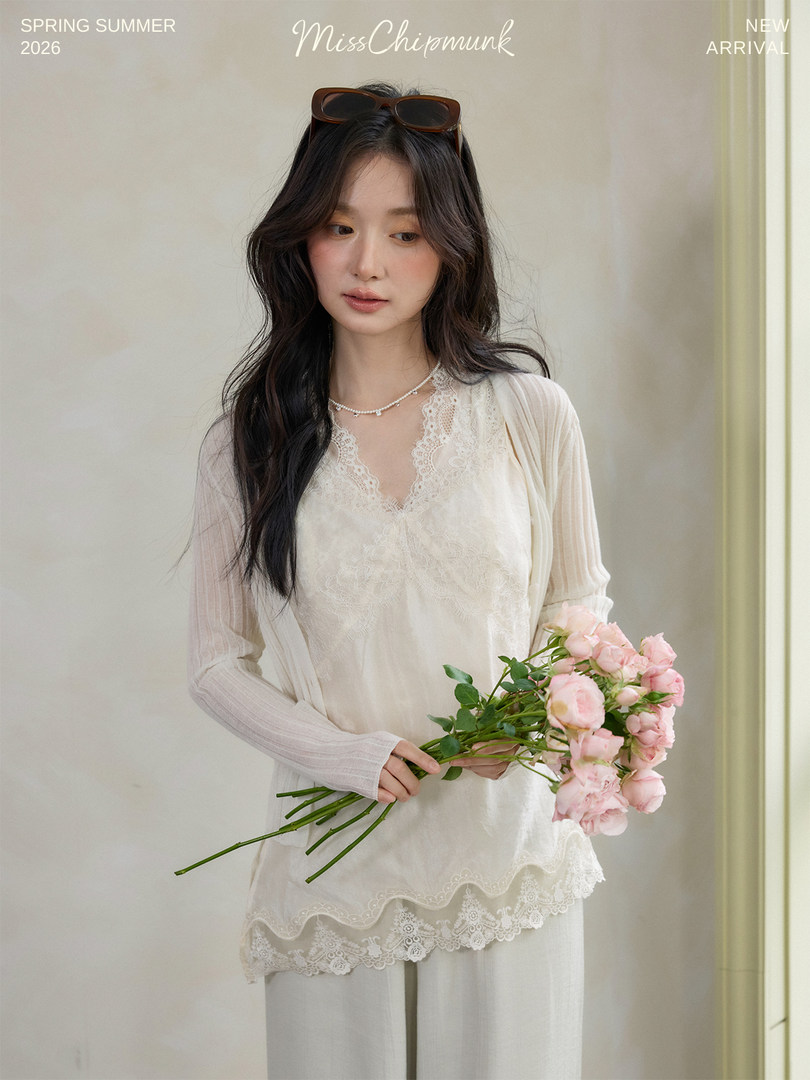 Woman wearing a cream lace-trim long-sleeve top with sheer sleeves and holding pink flowers
