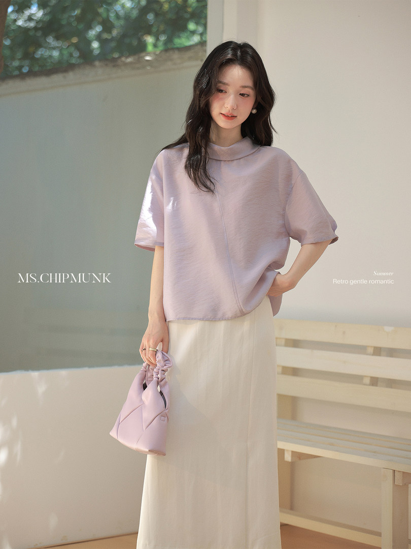 Woman wearing a lavender short-sleeve top and cream skirt with a matching handbag