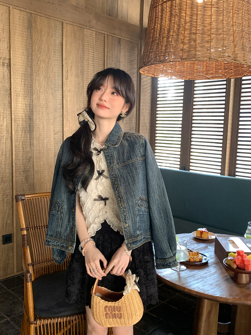 Woman wearing a blue denim jacket over a white top and black skirt while holding a woven handbag
