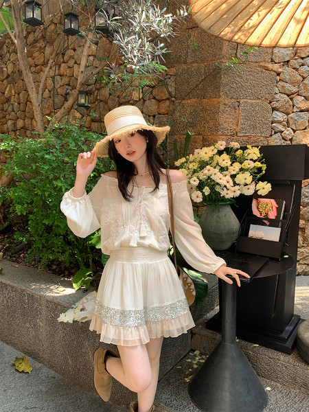 Woman wearing a cream off-shoulder blouse and ruffled skirt with a straw hat outdoors