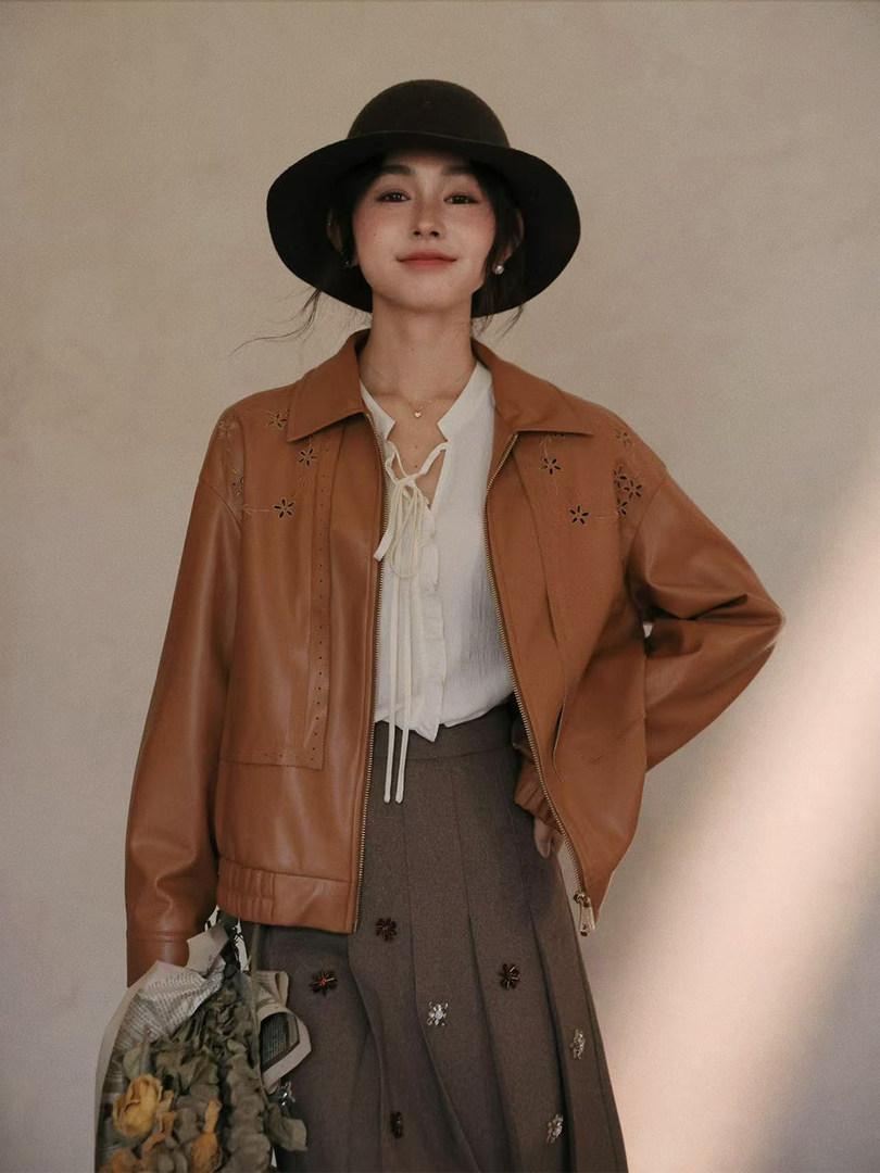 Model wearing a brown faux leather jacket with a white blouse and black hat