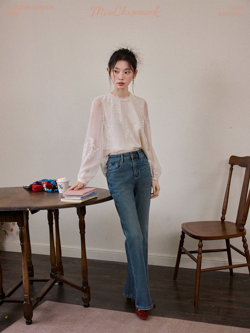 Model wearing a sheer long-sleeve blouse with blue jeans in a studio setting