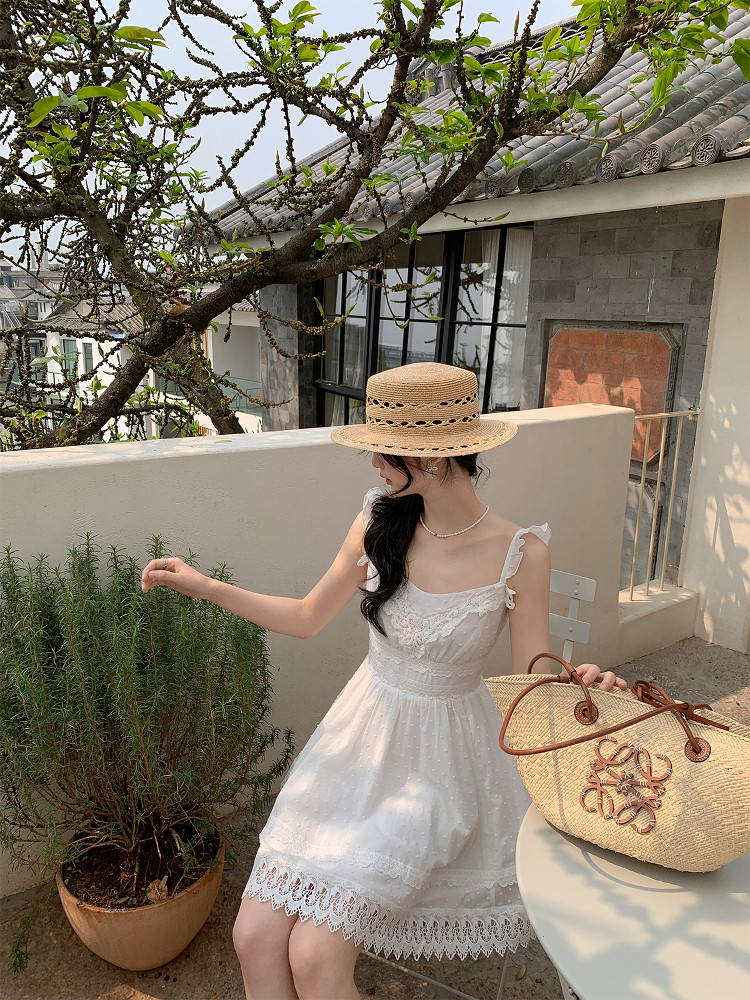 Woman wearing a white lace summer dress and straw hat with a woven handbag outdoors