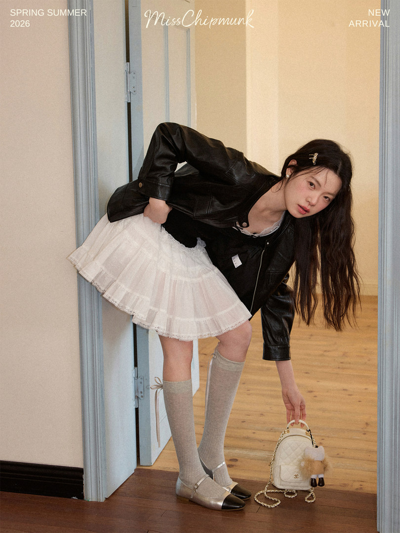 Model wearing a black leather jacket with a white pleated mini skirt and silver shoes
