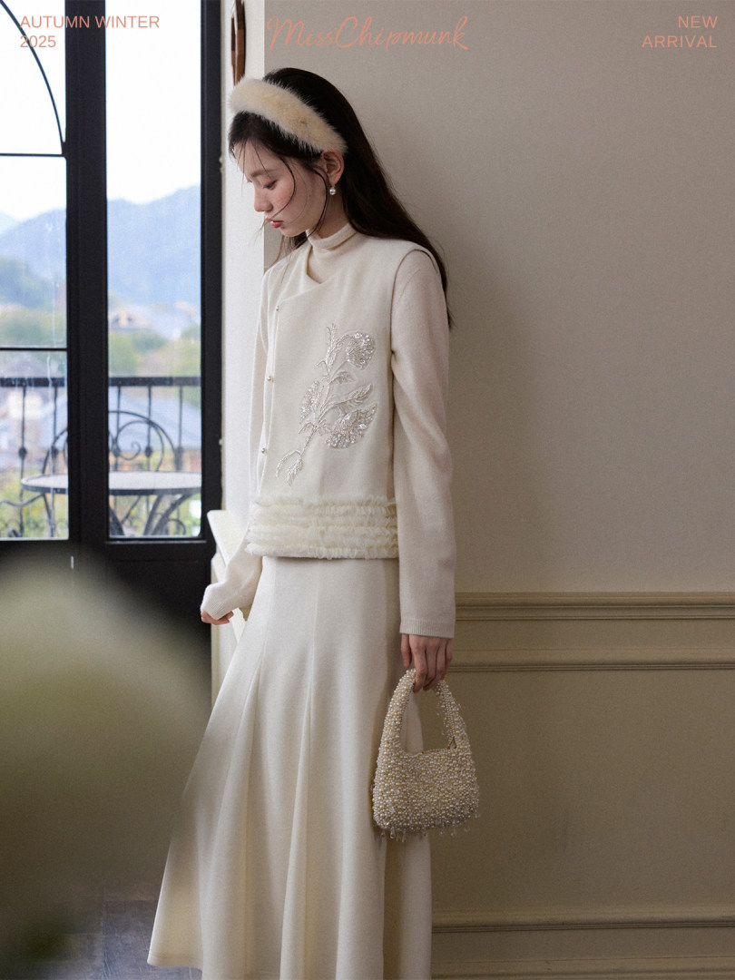 Model wearing a cream autumn-winter outfit with a beaded handbag
