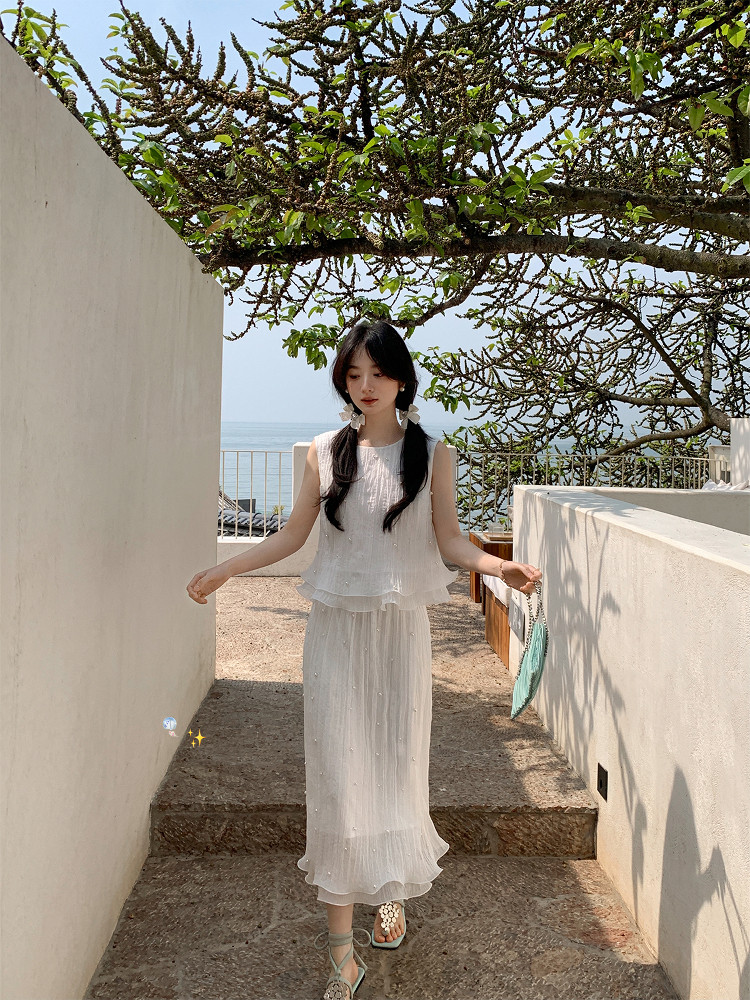 Woman wearing a white sleeveless dress outdoors by the sea