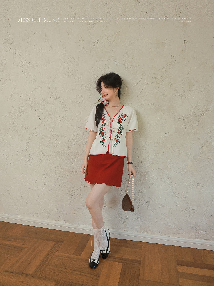 Woman wearing a white embroidered short-sleeve top with a red mini skirt and boots