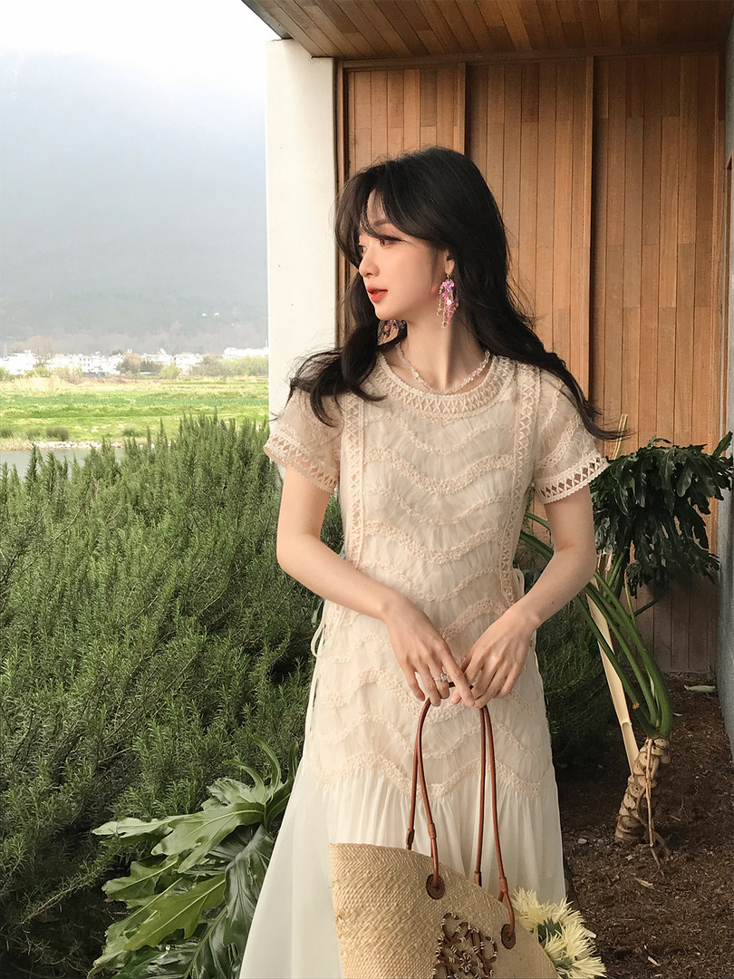 Woman wearing a cream lace dress and holding a woven tote bag outdoors
