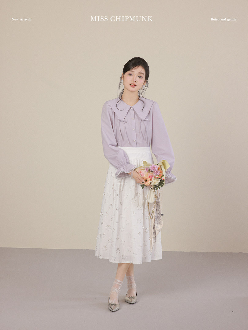 Young woman modeling a lavender blouse and white floral skirt with a bouquet on a neutral studio background