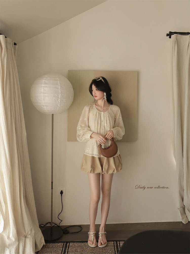 Woman wearing a cream blouse with beige shorts and sandals in a studio setting
