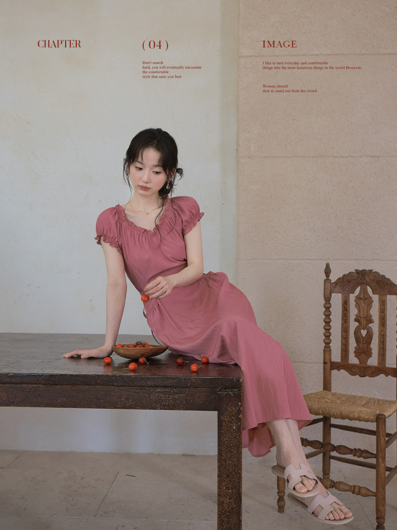 Woman wearing a pink dress seated on a table in a studio setting