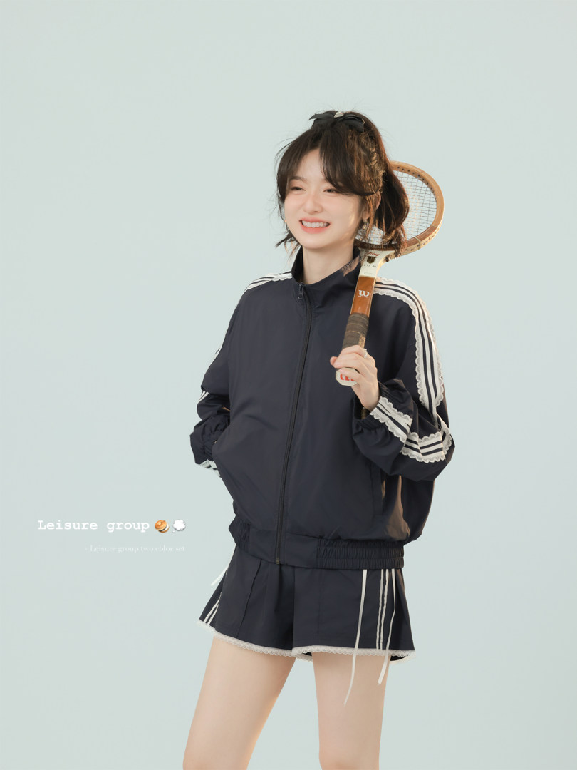 Woman wearing a black sporty track jacket and shorts set holding a tennis racket