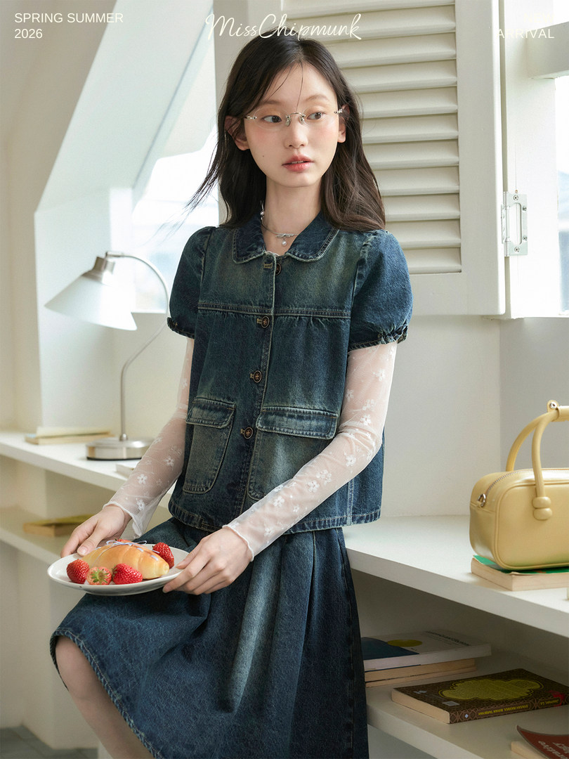 Model wearing a dark denim vest and skirt set with sheer floral sleeves