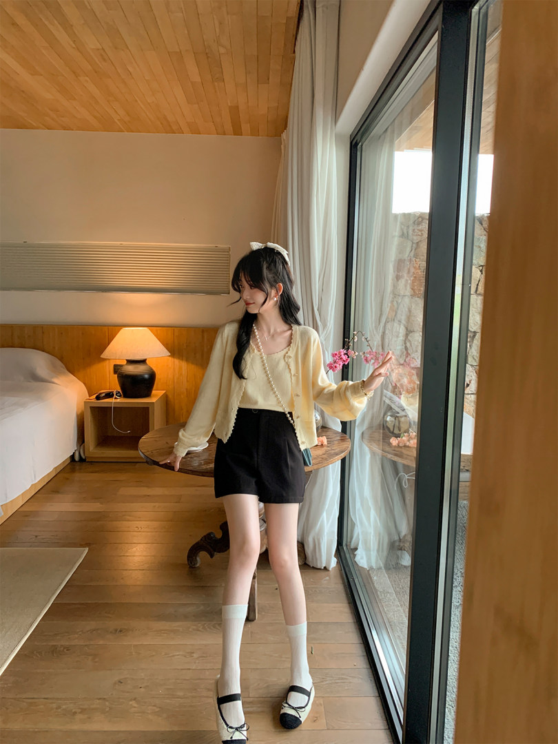 Woman wearing a light cream cardigan and black shorts outfit