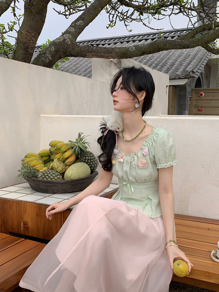 Woman wearing a pastel green puff-sleeve top with a pink sheer skirt outdoors