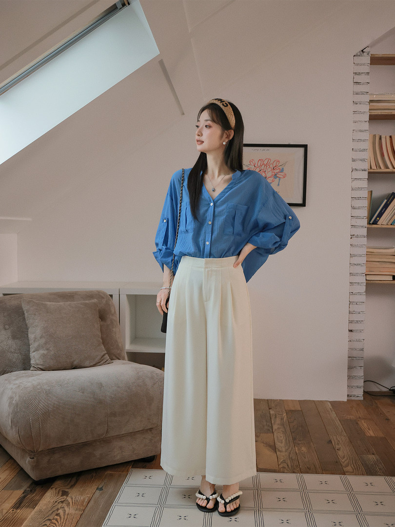 Woman wearing a blue loose blouse with cream wide-leg pants and black sandals