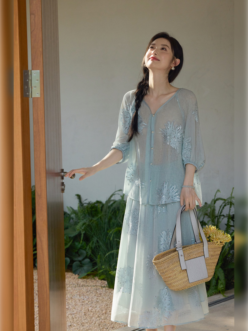 Model wearing a light blue embroidered dress set and carrying a straw tote bag