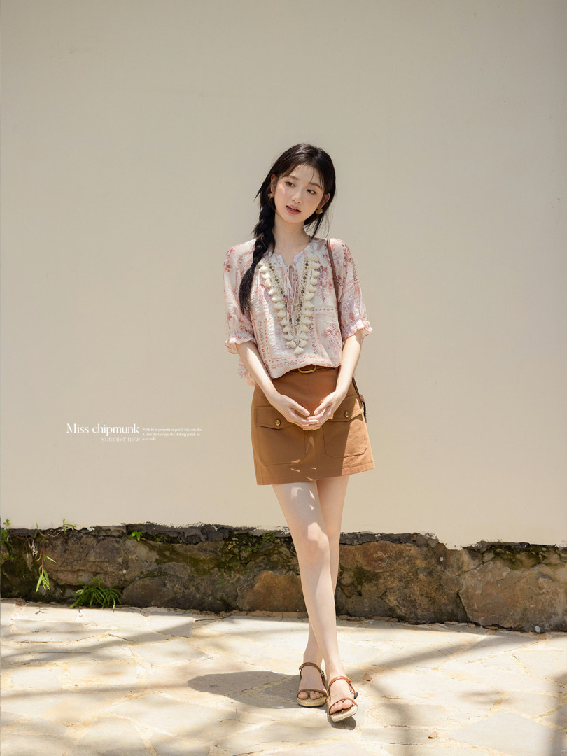 Woman wearing a sheer floral blouse with a brown mini skirt and sandals outdoors