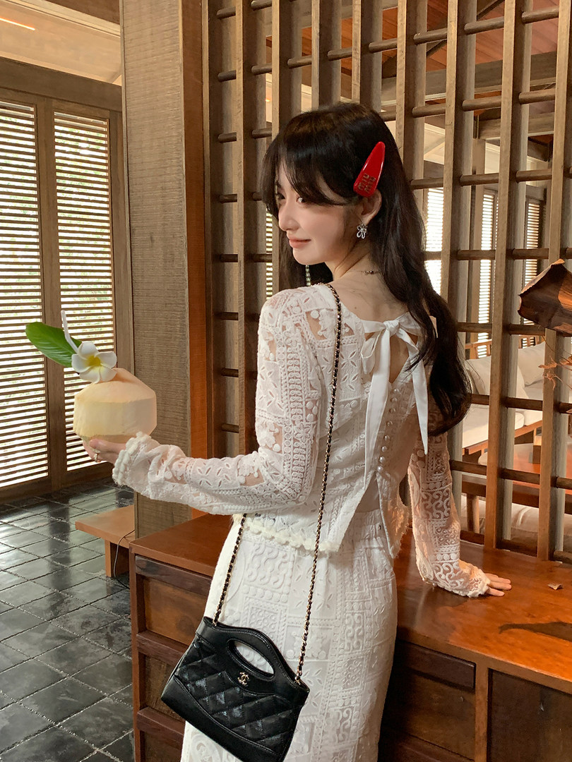 Woman wearing a white lace dress with a black quilted handbag