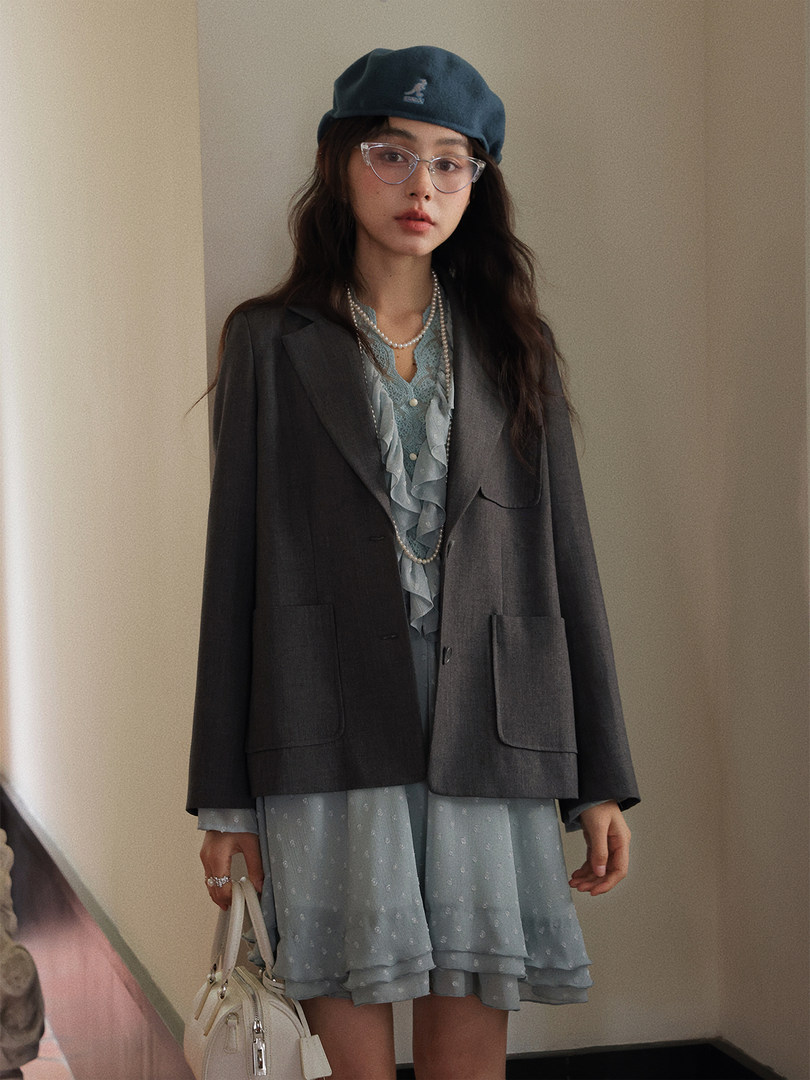 Fashion model wearing a dark blazer over a light blue dress with a beret and handbag