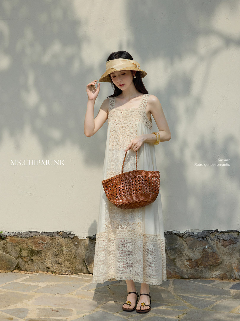 Model wearing a cream lace maxi dress with a straw hat and woven bag outdoors