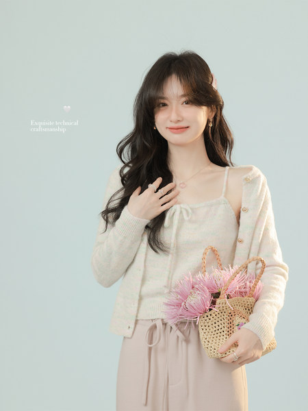Woman wearing a cream knit cardigan and matching top, holding a woven handbag