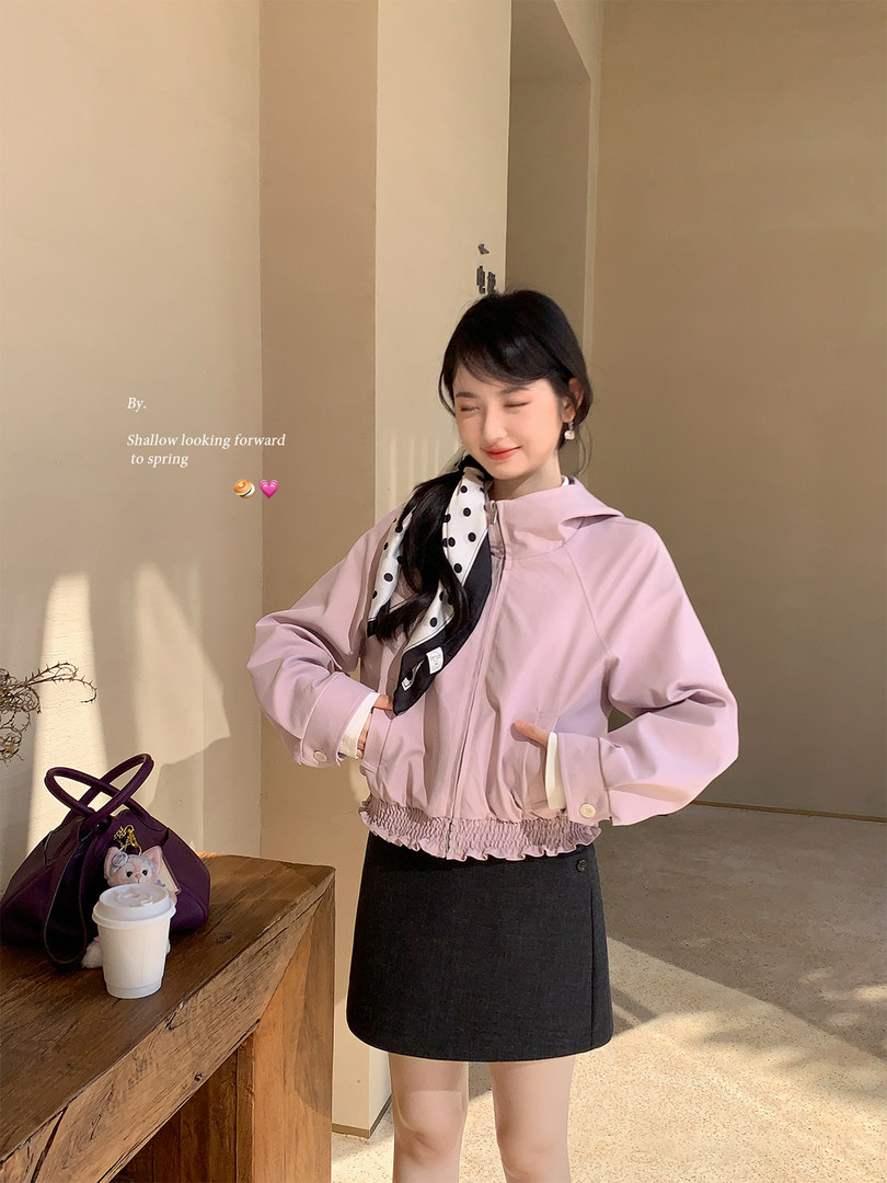 Model wearing a light pink zip-up jacket with a black skirt indoors
