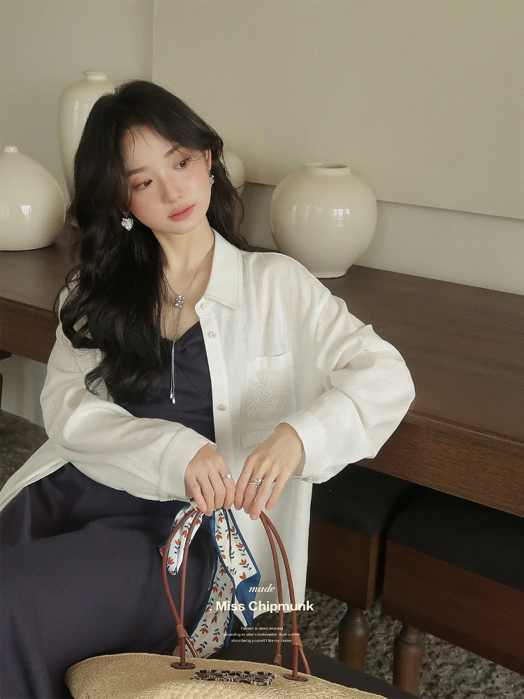 Woman wearing a white oversized shirt over a navy dress and holding a woven handbag