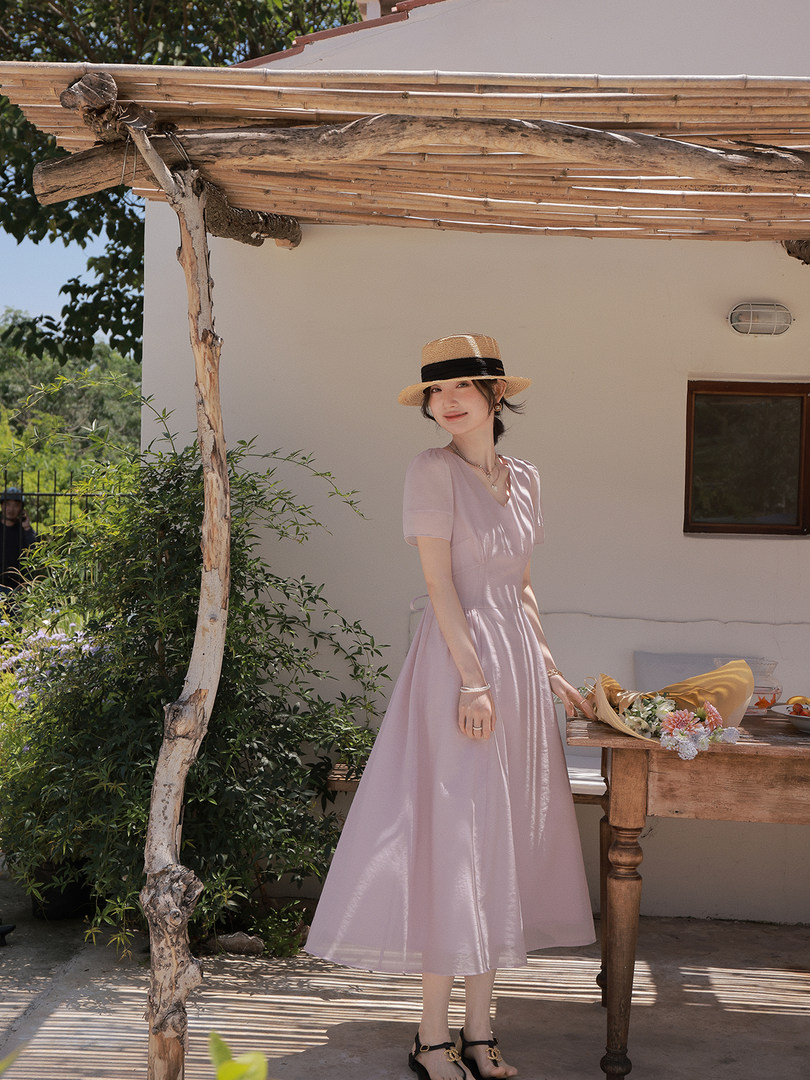 Woman wearing a light pink midi dress and straw hat outdoors