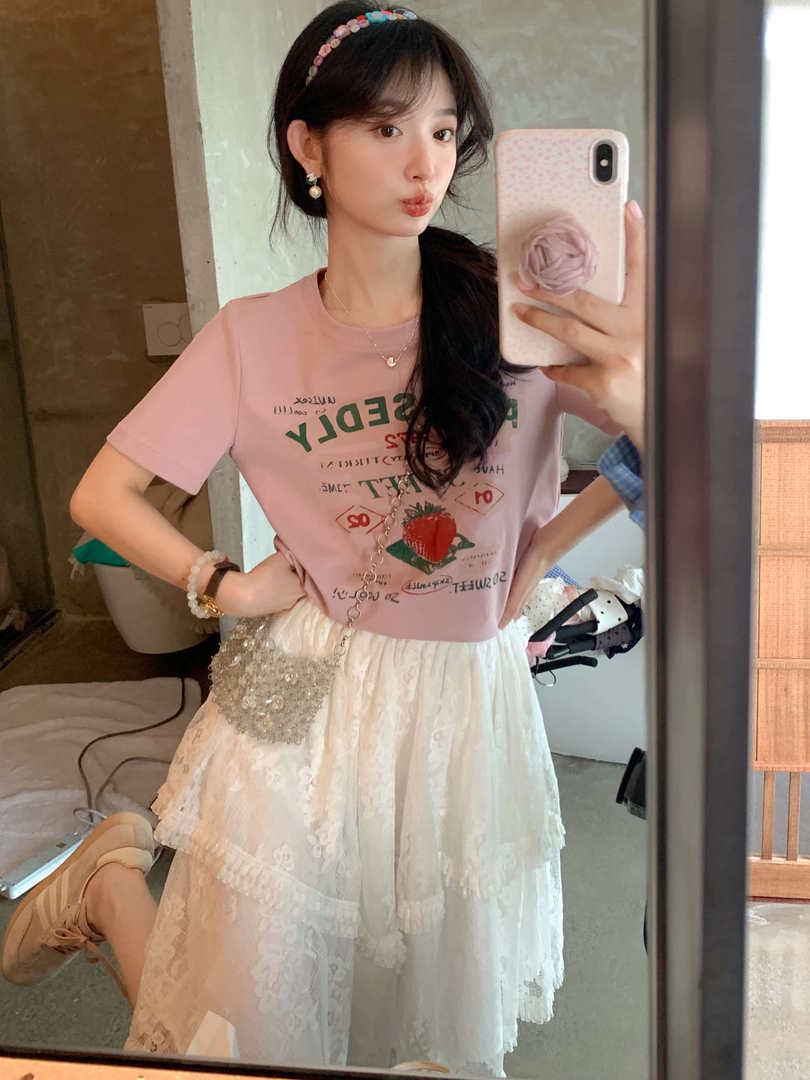 Woman wearing a pink graphic T-shirt and white lace skirt in a mirror selfie