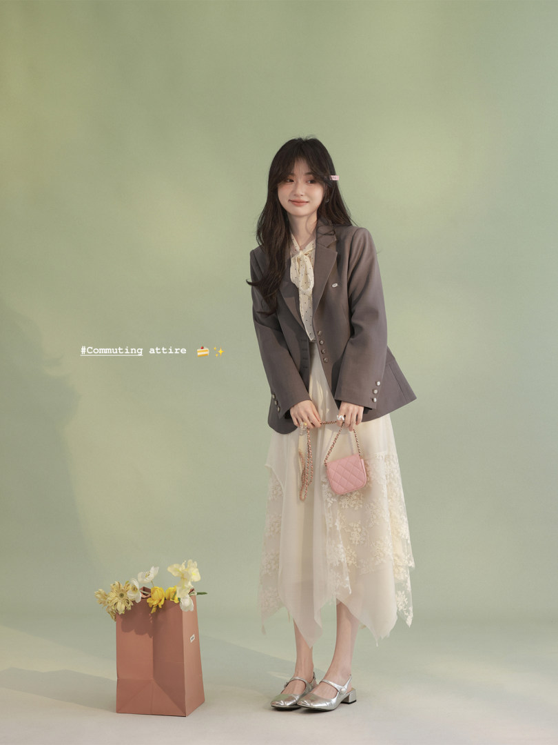 Woman wearing a brown blazer over a cream lace dress with a small pink quilted bag
