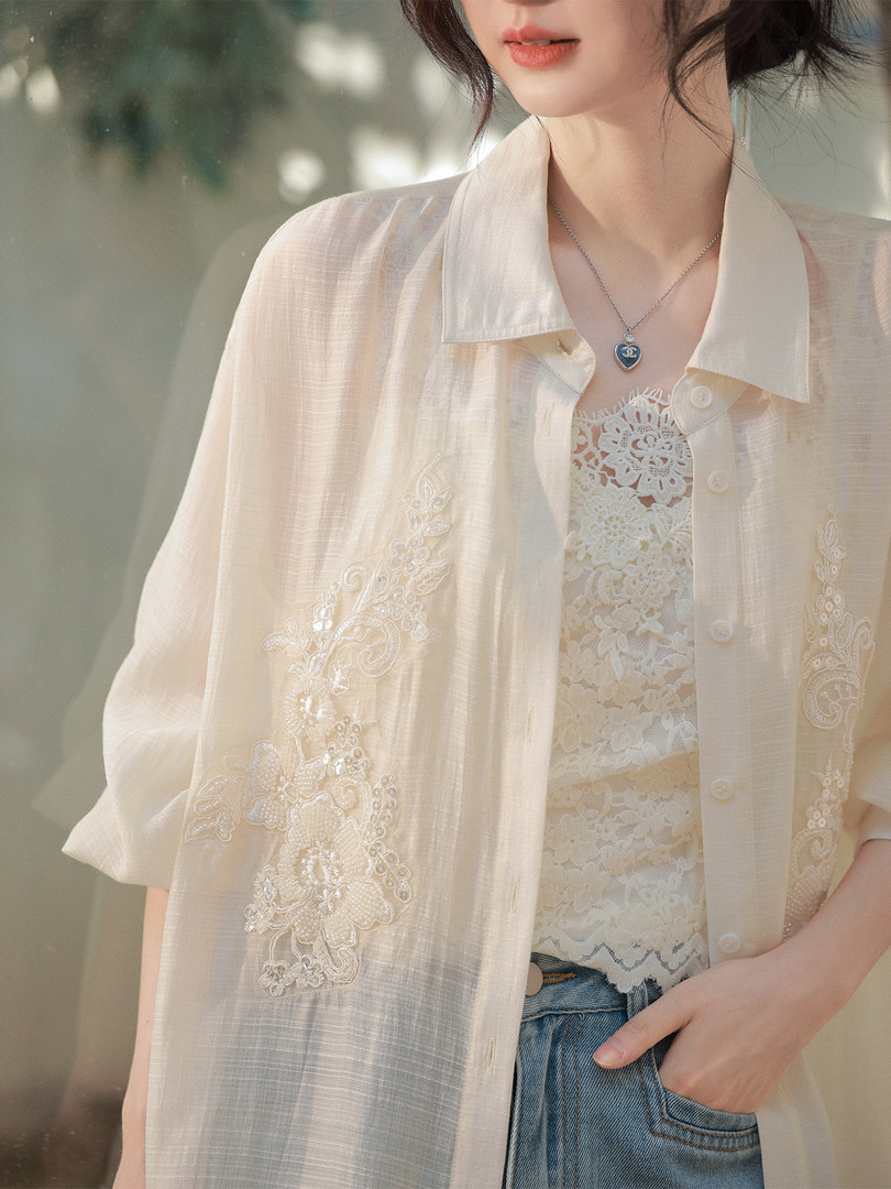 Woman wearing a sheer embroidered cream blouse over a lace top