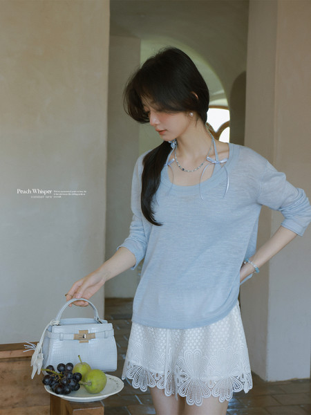 Woman wearing a light blue long-sleeve top with a white lace mini skirt and holding a light blue handbag