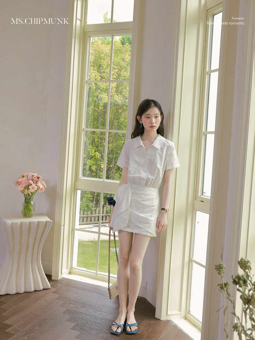 Model wearing a white short-sleeve blouse and mini skirt in a bright indoor setting