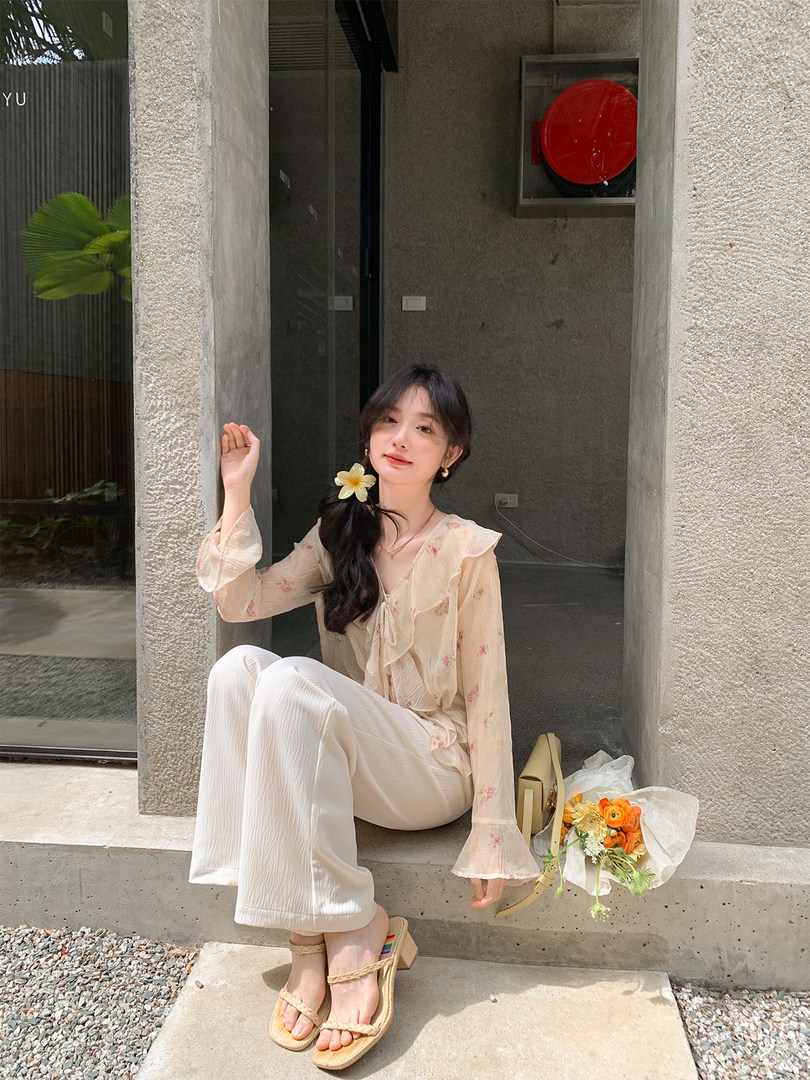 Model wearing a light floral blouse with white wide-leg pants and sandals outdoors