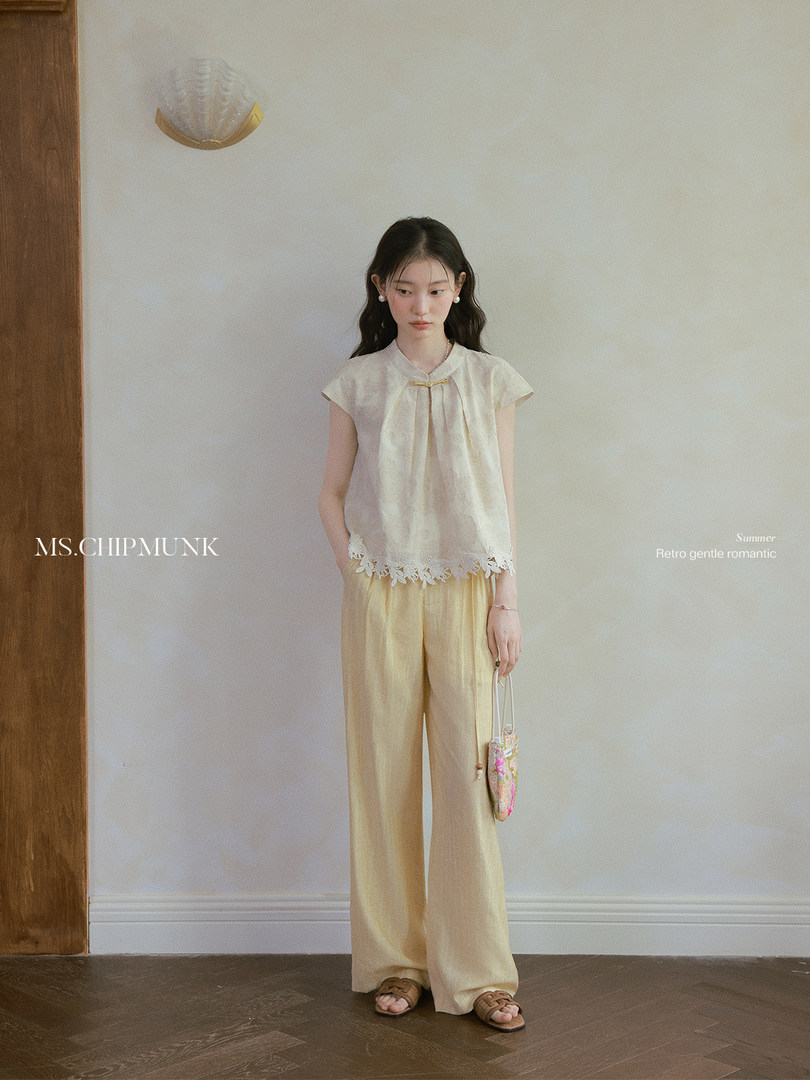 Woman wearing a light beige summer outfit with floral-trimmed top and wide-leg pants