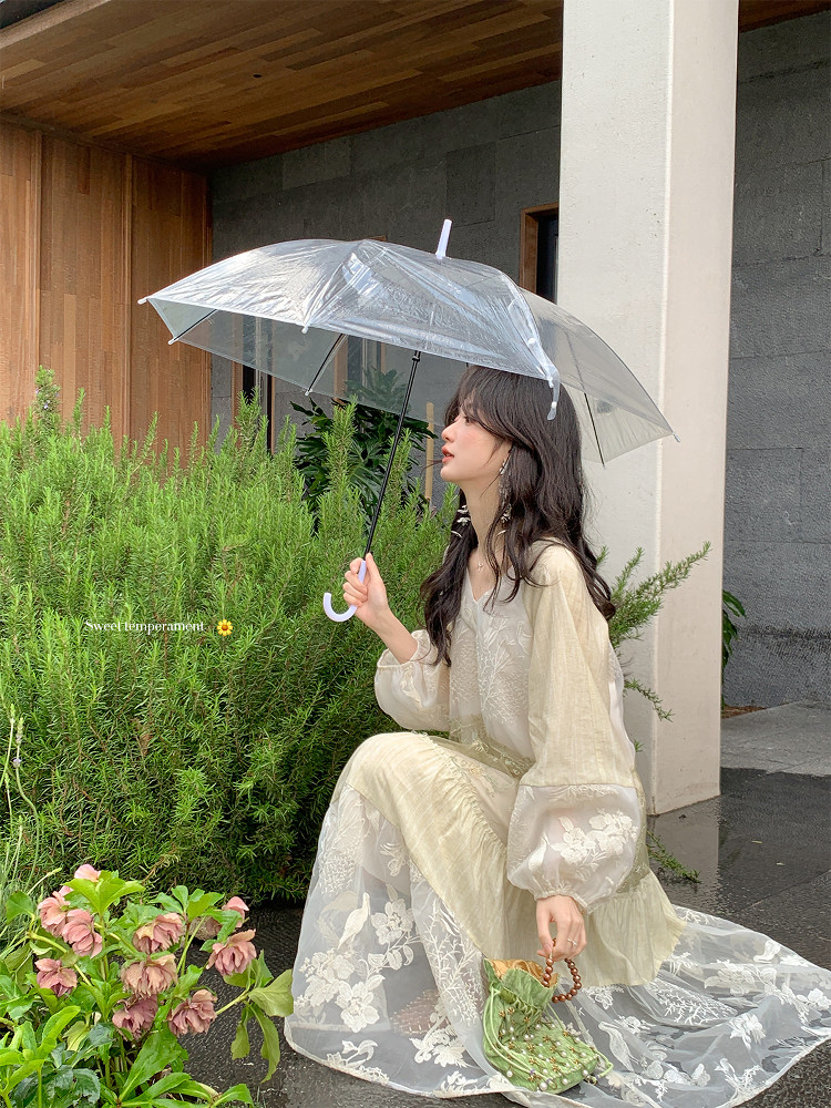 Woman wearing a sheer floral long dress while holding a transparent umbrella outdoors