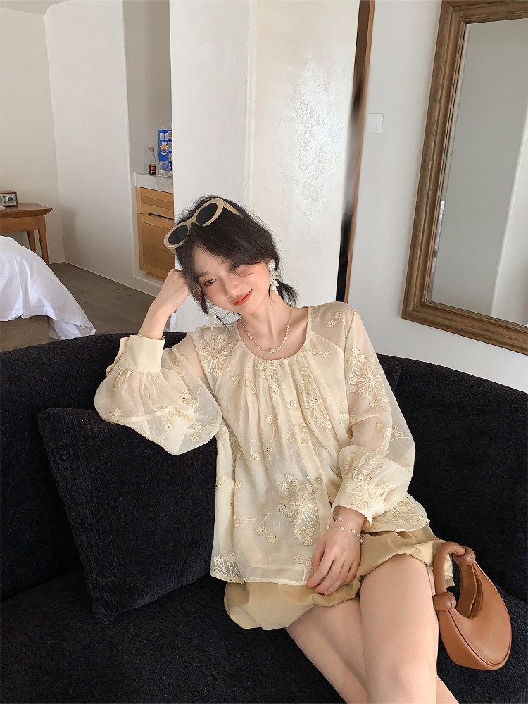 Woman wearing a sheer embroidered cream blouse and tan skirt while sitting on a black sofa
