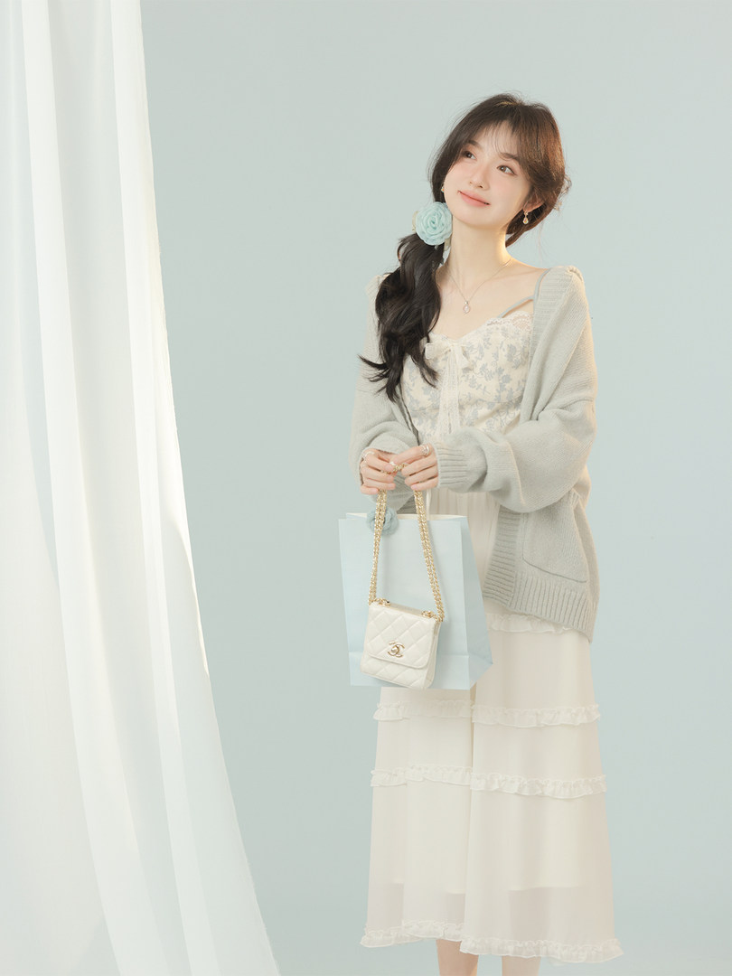 Woman modeling a cream lace dress with a light cardigan and small chain handbag