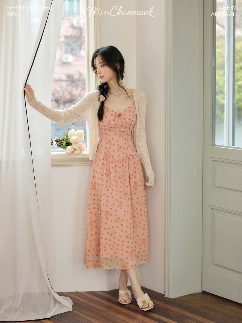 Woman wearing a pink polka dot dress with a light cardigan indoors