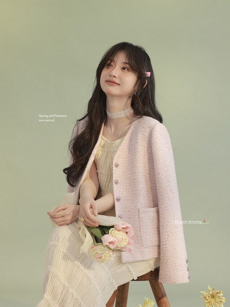 Model wearing a pastel pink textured jacket over a cream dress, holding flowers