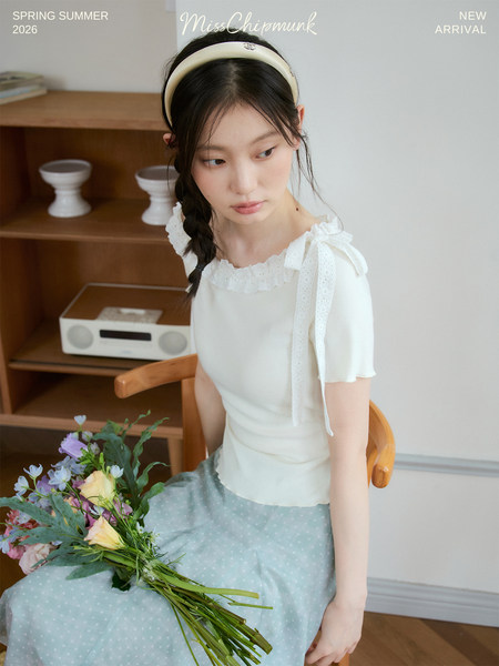 Woman wearing a white ruffled top and light blue skirt while holding flowers