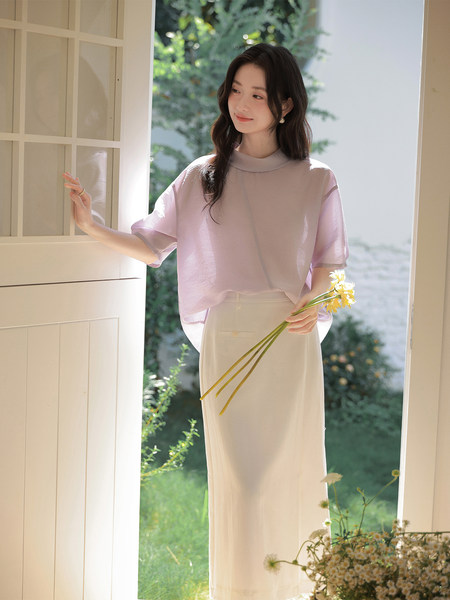 Woman wearing a light lavender blouse with a cream skirt in a bright doorway
