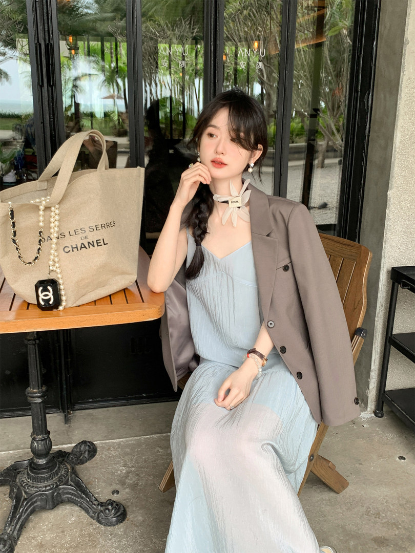 Woman wearing a light blue dress with a gray blazer, seated outdoors with a beige tote bag