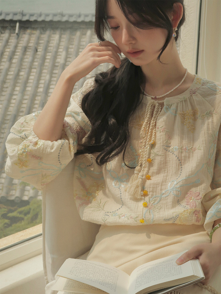 Light embroidered cream blouse worn by a model indoors