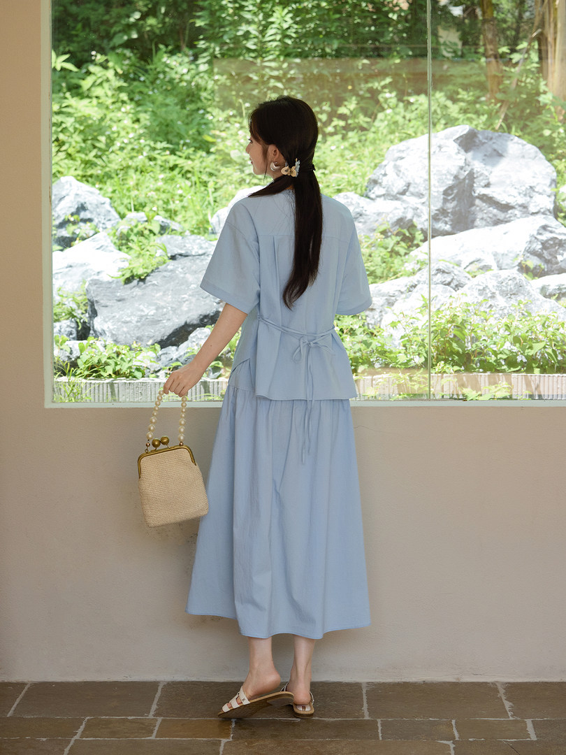 Woman wearing a light blue two-piece dress with a woven handbag