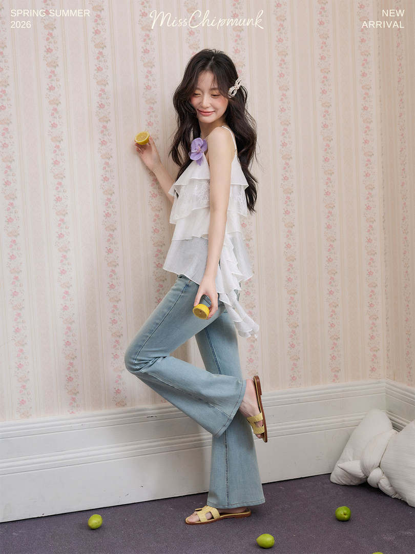 Model wearing a white ruffled sleeveless top with light flared jeans in a spring fashion promo image